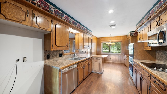 kitchen with appliances with stainless steel finishes, brown cabinets, a sink, and wood finished floors