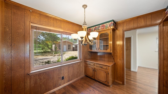 unfurnished dining area with wood walls, baseboards, dark wood finished floors, and an inviting chandelier