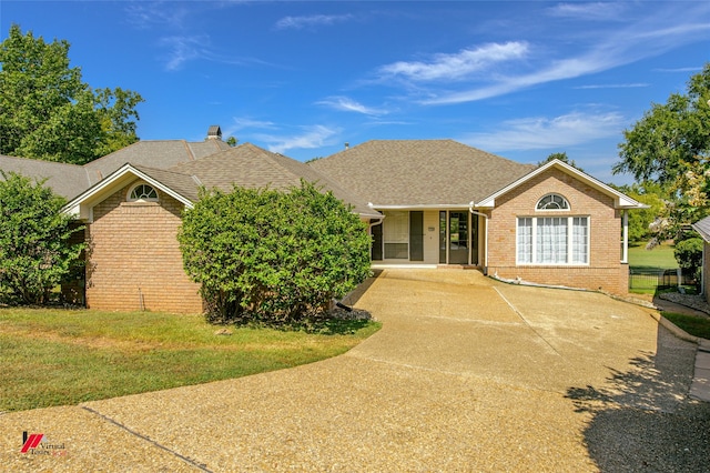 ranch-style home featuring a shingled roof, a front yard, and brick siding