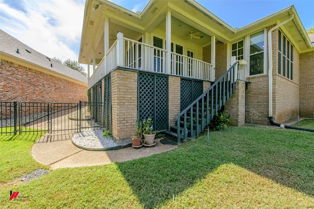 view of side of home with a yard, stairway, a ceiling fan, and brick siding