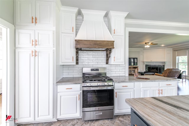 kitchen featuring ornamental molding, open floor plan, stainless steel gas stove, white cabinetry, and premium range hood