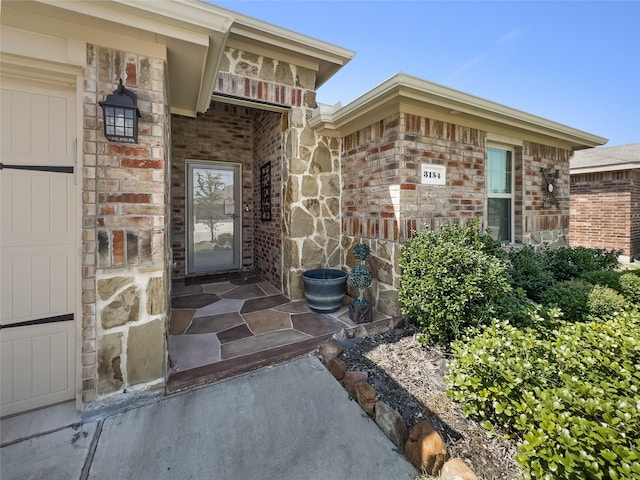 doorway to property with a garage, stone siding, and brick siding