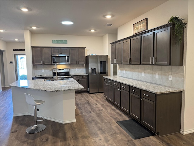 kitchen featuring stainless steel appliances, a sink, visible vents, light stone countertops, and a center island with sink