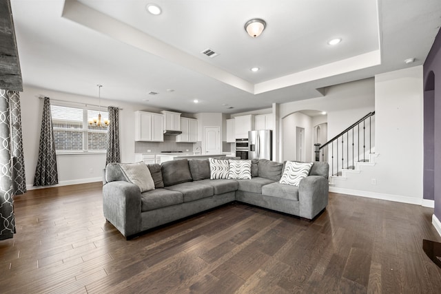 living room with an inviting chandelier, dark hardwood / wood-style floors, and a raised ceiling