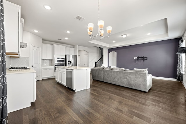 kitchen with stainless steel appliances, an island with sink, hanging light fixtures, dark hardwood / wood-style floors, and white cabinets