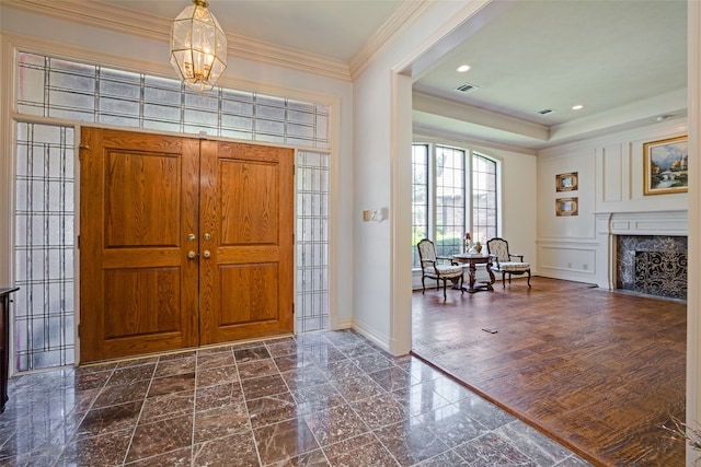 entryway featuring dark hardwood / wood-style floors, an inviting chandelier, crown molding, and a premium fireplace