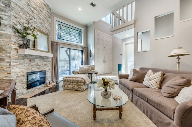 living room featuring a high ceiling, ornamental molding, and a stone fireplace