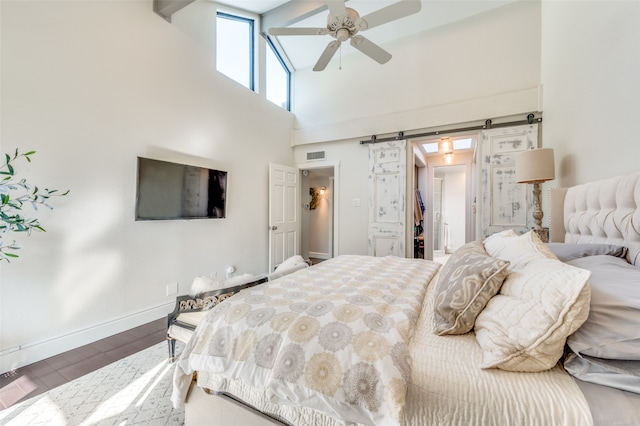 bedroom featuring hardwood / wood-style floors, a towering ceiling, connected bathroom, ceiling fan, and a barn door