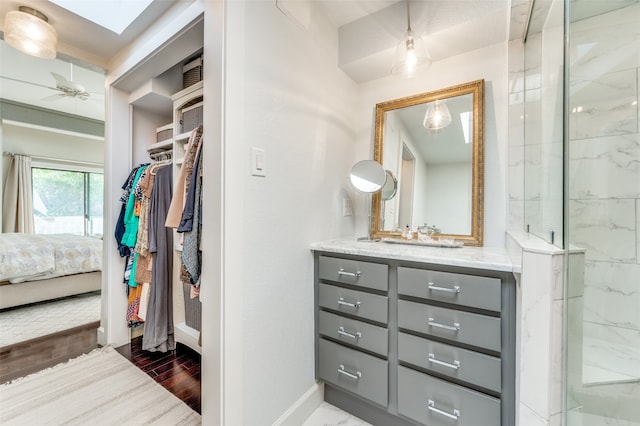 bathroom with a skylight, vanity, an enclosed shower, wood-type flooring, and ceiling fan