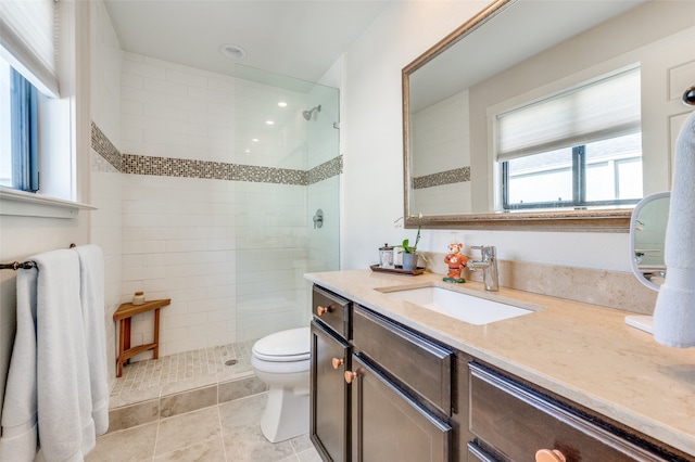 bathroom with tile patterned flooring, toilet, a tile shower, and vanity