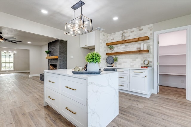 kitchen with light stone countertops, ceiling fan, a brick fireplace, a kitchen island, and white cabinetry