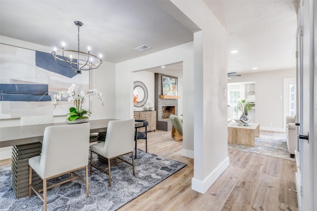 dining room featuring a brick fireplace, an inviting chandelier, and light hardwood / wood-style floors