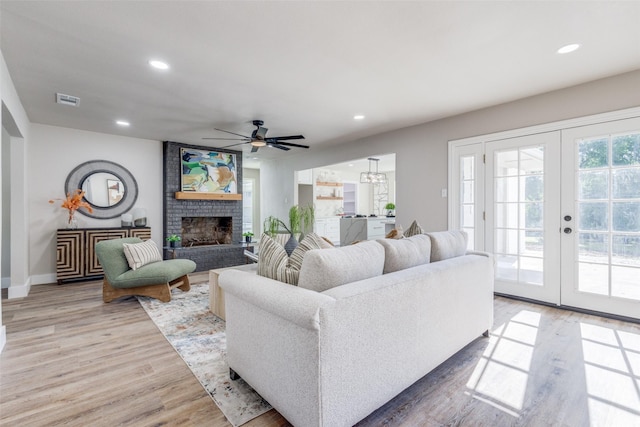 living room featuring ceiling fan, french doors, light wood-type flooring, and a fireplace