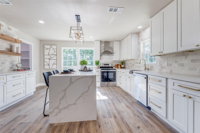 kitchen featuring wall chimney exhaust hood, pendant lighting, stainless steel appliances, white cabinets, and sink