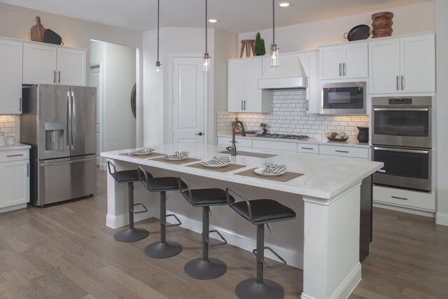 kitchen featuring a center island with sink, white cabinetry, stainless steel appliances, sink, and decorative light fixtures