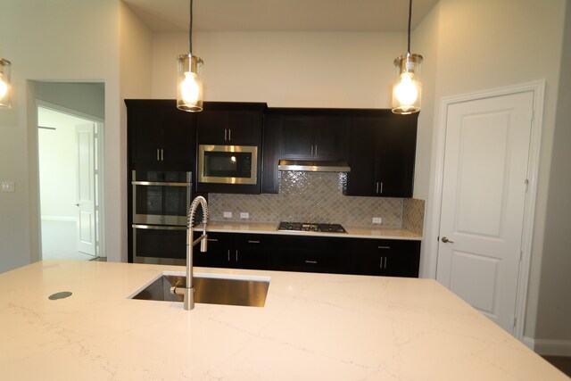 kitchen with hanging light fixtures, sink, appliances with stainless steel finishes, light stone counters, and tasteful backsplash