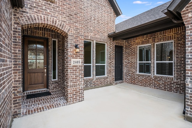 property entrance featuring brick siding and a shingled roof