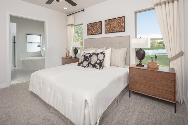 carpeted bedroom featuring connected bathroom, ceiling fan, a water view, and multiple windows