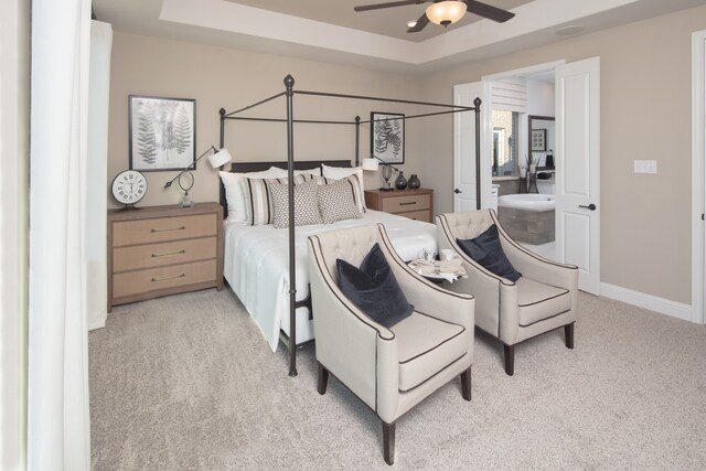 bedroom featuring light carpet, a tray ceiling, connected bathroom, and ceiling fan