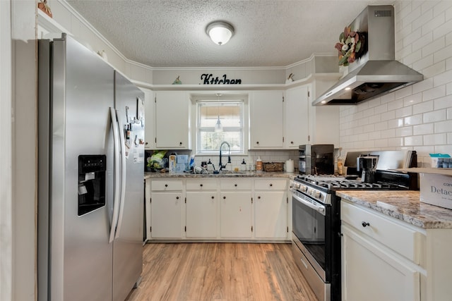 kitchen featuring white cabinets, wall chimney range hood, stainless steel appliances, ornamental molding, and light stone countertops