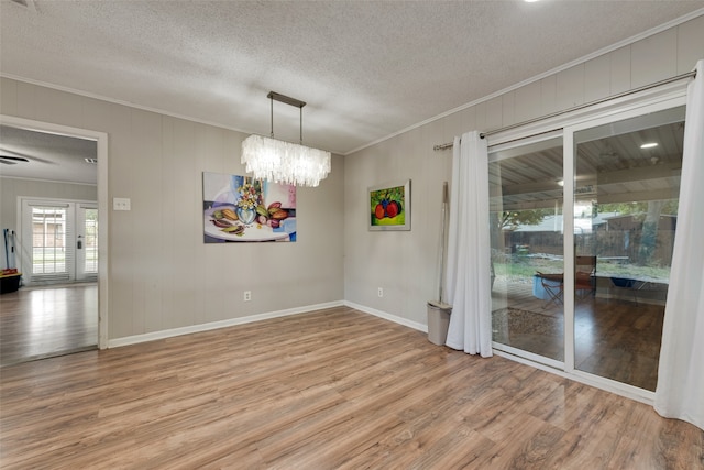 empty room with wood-type flooring, a textured ceiling, crown molding, and a chandelier