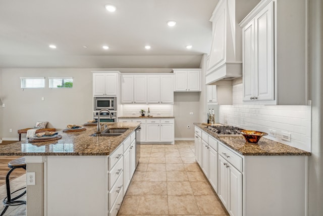 kitchen with tasteful backsplash, an island with sink, custom exhaust hood, white cabinets, and stainless steel appliances