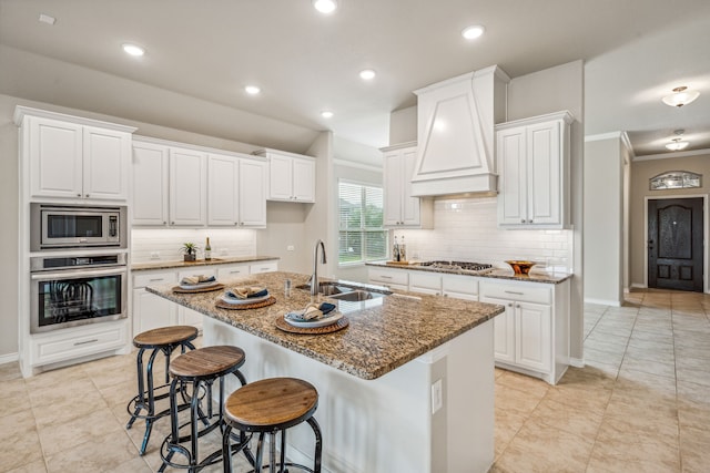 kitchen with decorative backsplash, a center island with sink, custom range hood, and stainless steel appliances