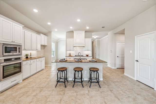 kitchen featuring tasteful backsplash, an island with sink, white cabinetry, appliances with stainless steel finishes, and stone counters