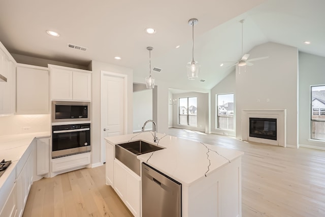 kitchen featuring sink, appliances with stainless steel finishes, lofted ceiling, and a center island with sink