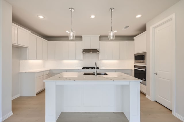 kitchen featuring white cabinetry, a kitchen island with sink, pendant lighting, light hardwood / wood-style floors, and stainless steel appliances