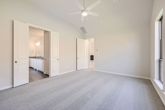 unfurnished bedroom featuring ceiling fan, ensuite bath, dark carpet, and vaulted ceiling