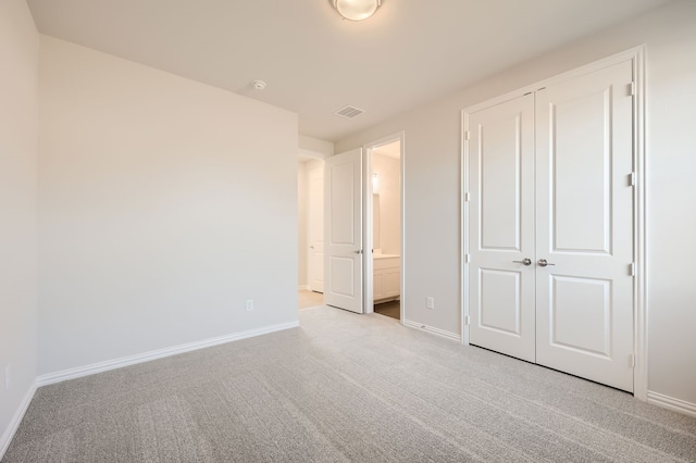 unfurnished bedroom featuring a closet, light carpet, and connected bathroom