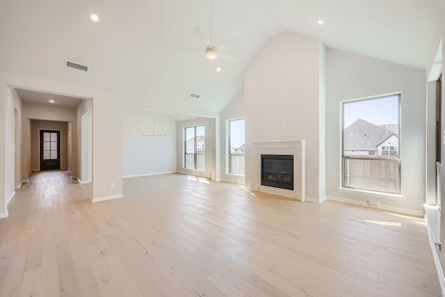 unfurnished living room featuring ceiling fan with notable chandelier, high vaulted ceiling, and light wood-type flooring