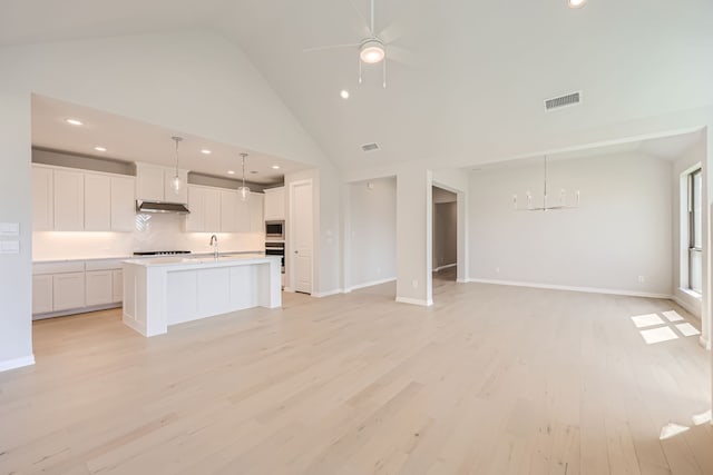 kitchen featuring white cabinets, an island with sink, high vaulted ceiling, light hardwood / wood-style floors, and stainless steel appliances