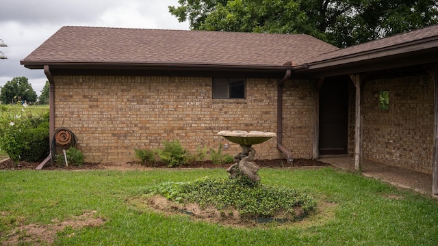 view of home's exterior with a yard, brick siding, and roof with shingles