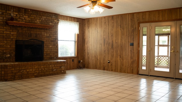 unfurnished living room featuring ceiling fan, wooden walls, light tile patterned floors, and a fireplace