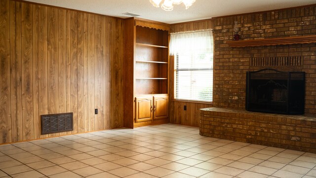 unfurnished living room with wood walls, built in features, a textured ceiling, a fireplace, and light tile patterned floors