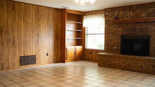 unfurnished living room featuring light tile patterned floors, a brick fireplace, visible vents, a textured ceiling, and wood walls