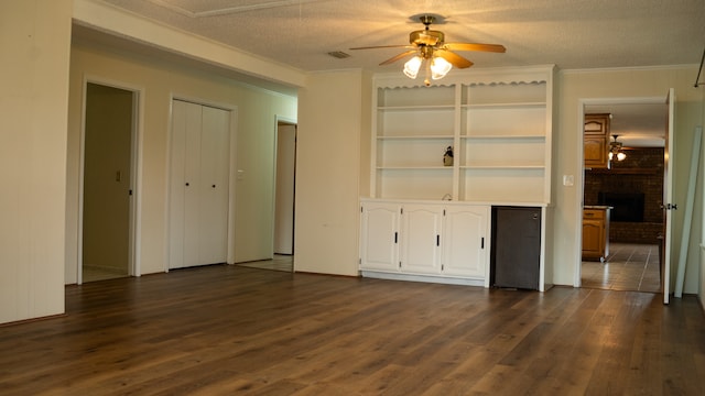 interior space featuring a brick fireplace, built in shelves, dark wood-type flooring, a textured ceiling, and ceiling fan