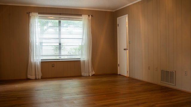 empty room with ornamental molding, wood finished floors, and visible vents