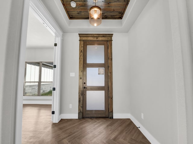 entryway with parquet flooring, a raised ceiling, and baseboards