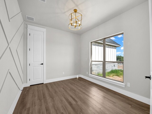 unfurnished room with an inviting chandelier, baseboards, dark wood-type flooring, and visible vents