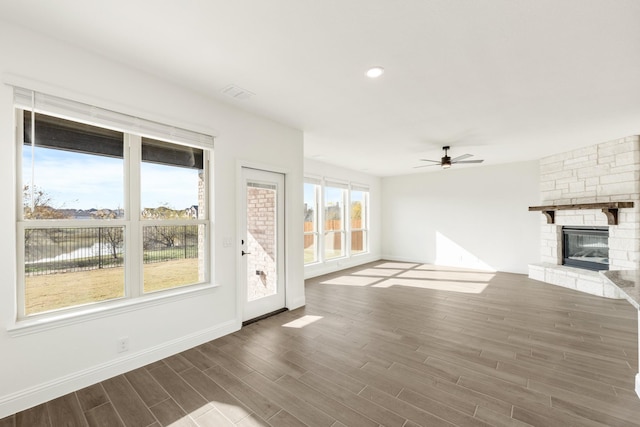 unfurnished living room with a water view, ceiling fan, a stone fireplace, and dark hardwood / wood-style flooring