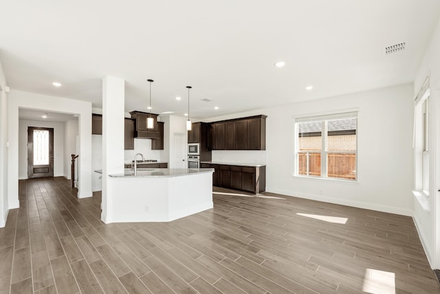 kitchen with hardwood / wood-style floors, hanging light fixtures, light stone countertops, appliances with stainless steel finishes, and dark brown cabinetry