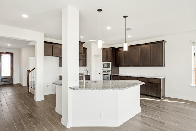 kitchen with light stone counters, sink, light hardwood / wood-style floors, oven, and hanging light fixtures