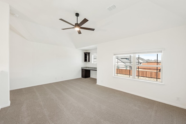 unfurnished living room featuring ceiling fan, light colored carpet, lofted ceiling, and built in desk