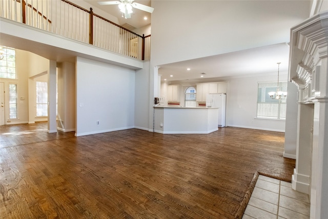 unfurnished living room with ceiling fan with notable chandelier, dark hardwood / wood-style flooring, and a high ceiling