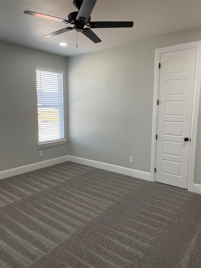 unfurnished room with ceiling fan and dark colored carpet