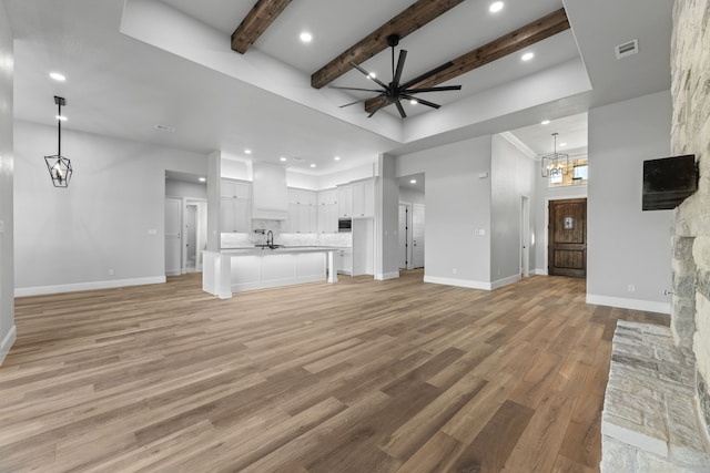 unfurnished living room featuring sink, beamed ceiling, light hardwood / wood-style flooring, and ceiling fan with notable chandelier