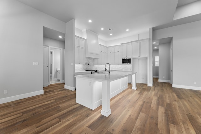 kitchen with dark hardwood / wood-style flooring, stainless steel microwave, white cabinetry, and an island with sink